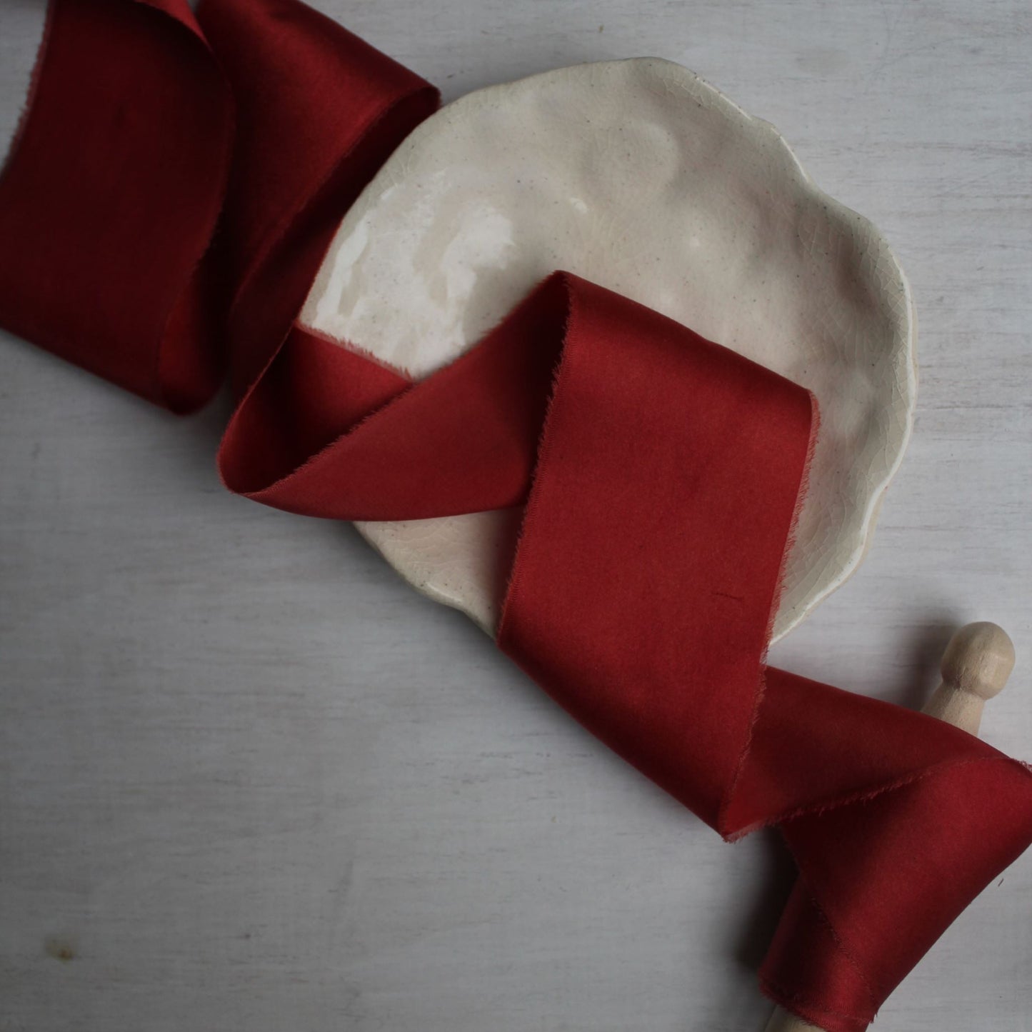 Christmas Red silk charmeuse ribbon hand torn, perfect for weddings, stationery, and decor, on a ceramic plate.