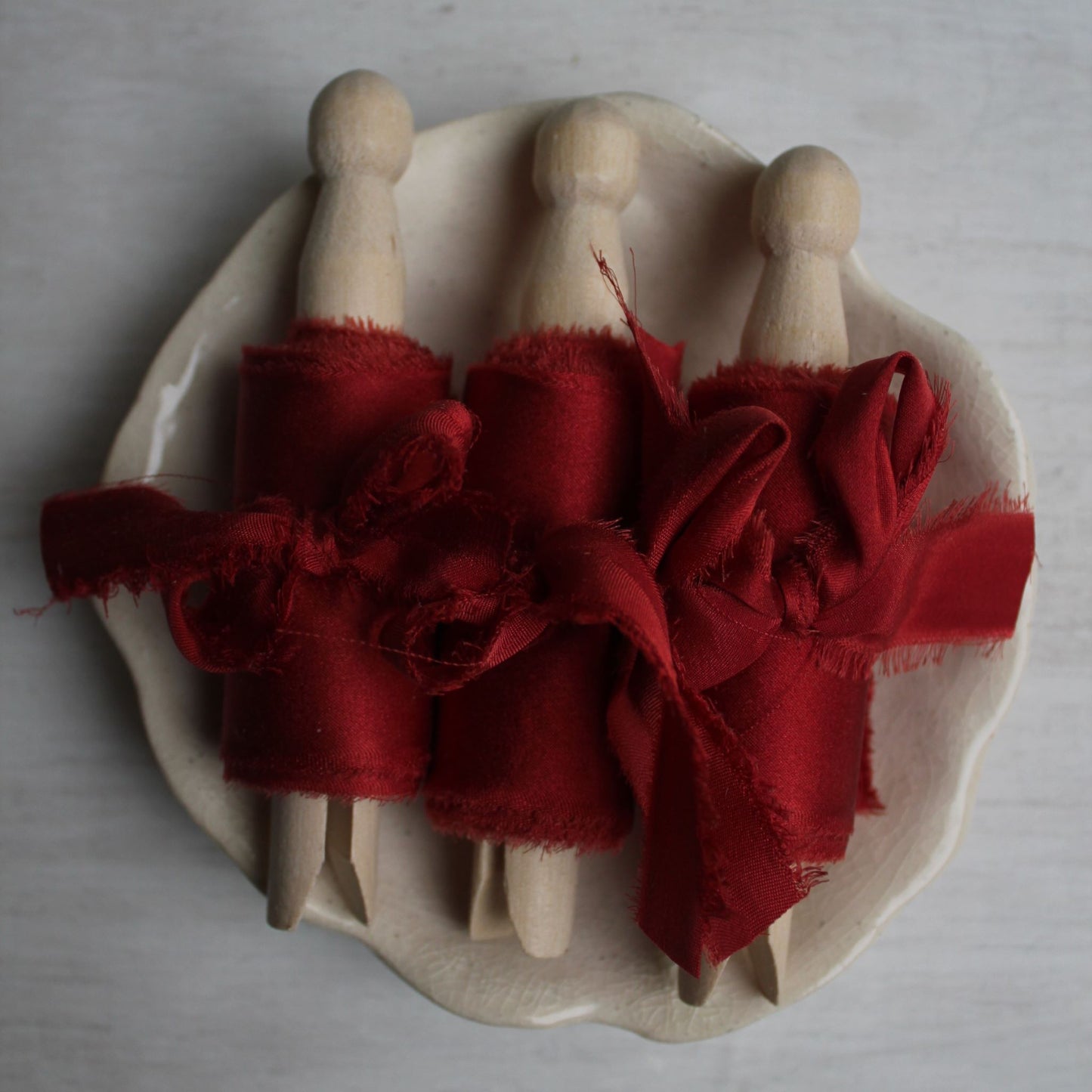 Christmas red silk charmeuse ribbon hand torn, displayed on a ceramic plate, perfect for weddings and décor.