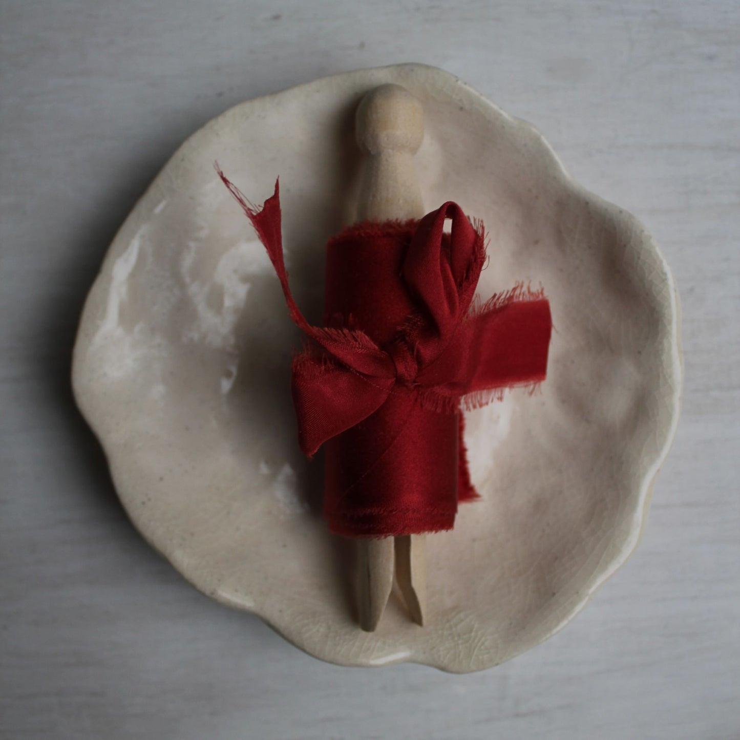 Christmas red silk charmeuse ribbon wrapped around a wooden figure, displayed on a handcrafted ceramic dish.