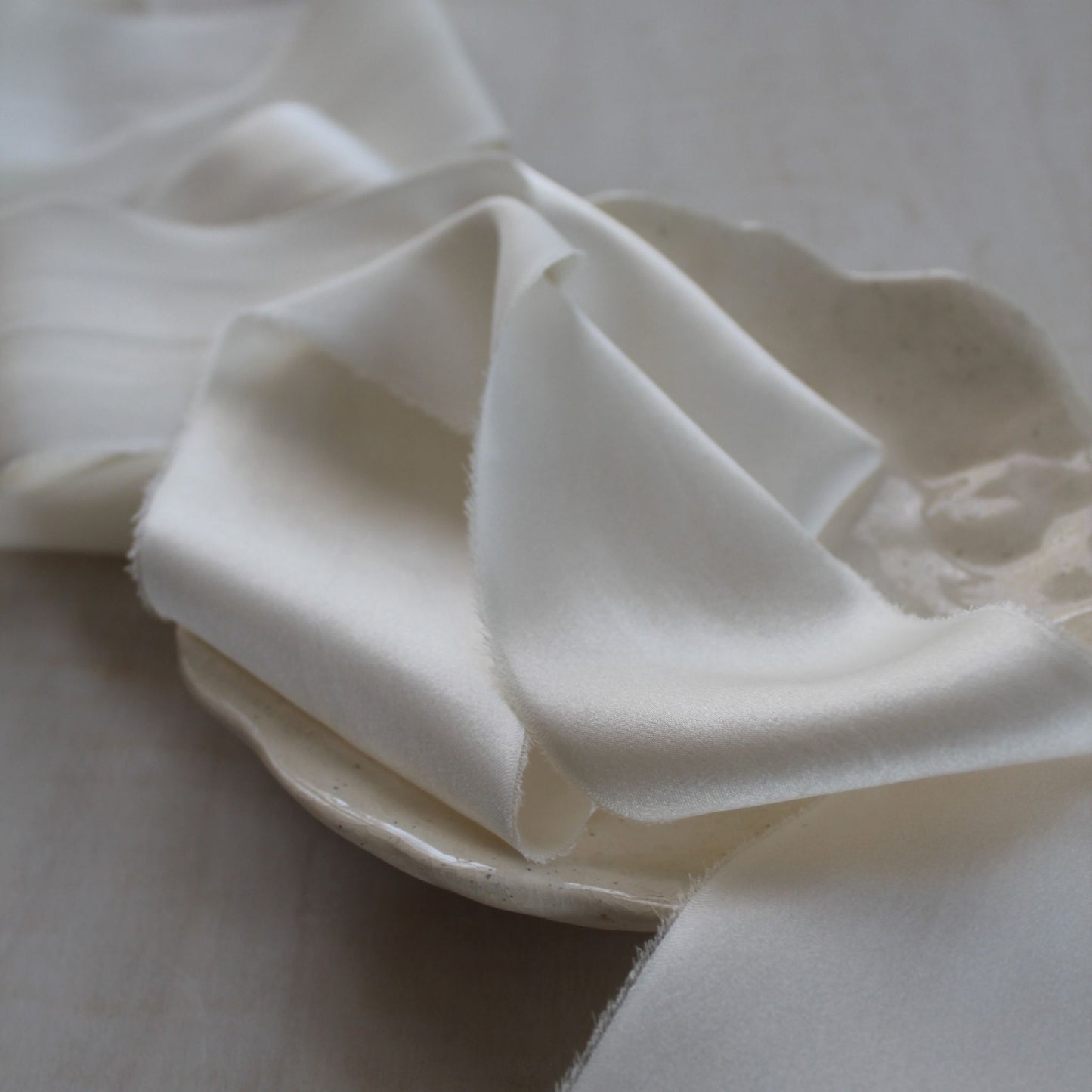 Close-up of hand-torn silk ribbon with frayed edge in soft white tone