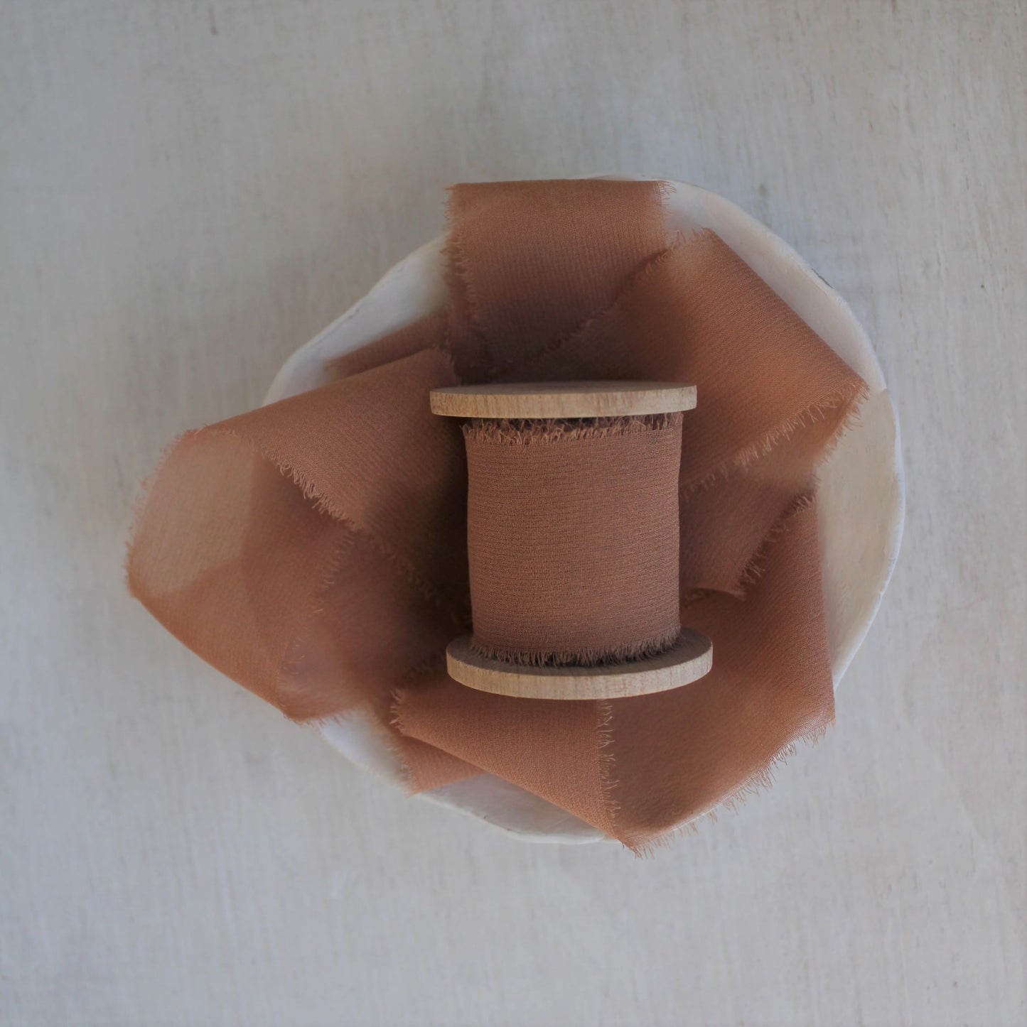 Hand-torn silk ribbon in terra cotta tone on wooden spool