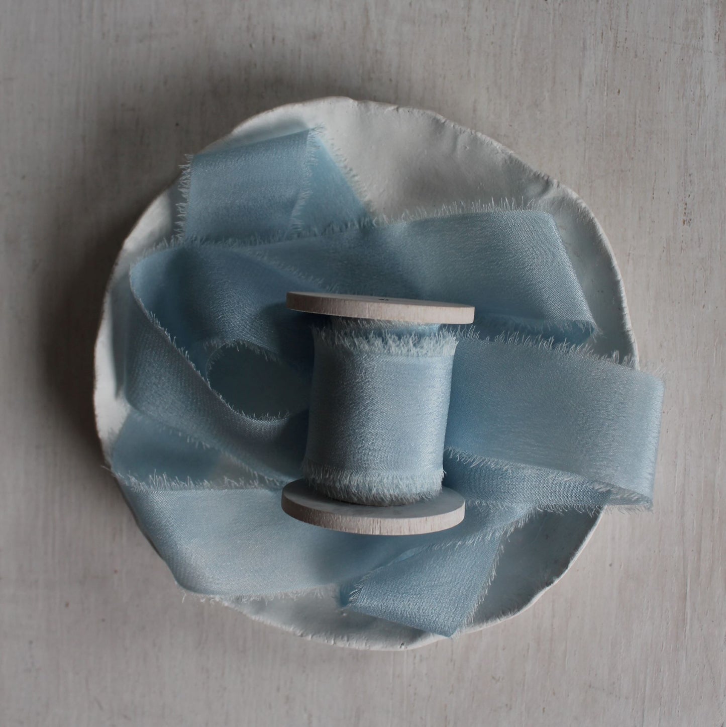 Hand-torn silk ribbon in pale blue for flatlay styling on wood spool