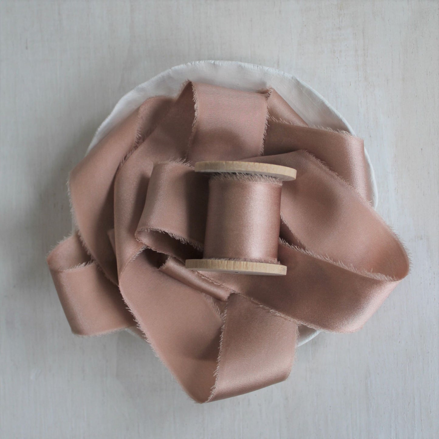 Dusty rose silk charmeuse hand-torn ribbon on wooden spool.
