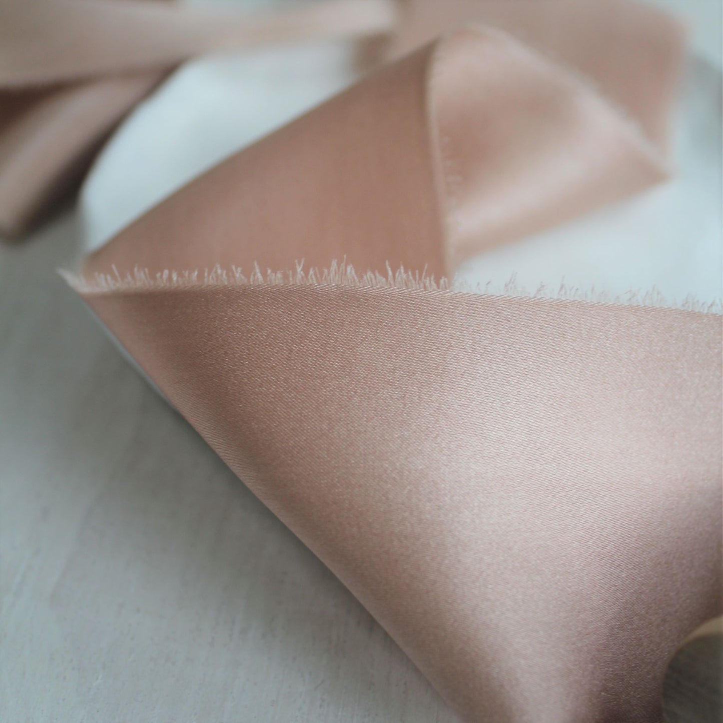 Close-up of hand-torn dusty rose silk charmeuse ribbon showcasing feathered edges.