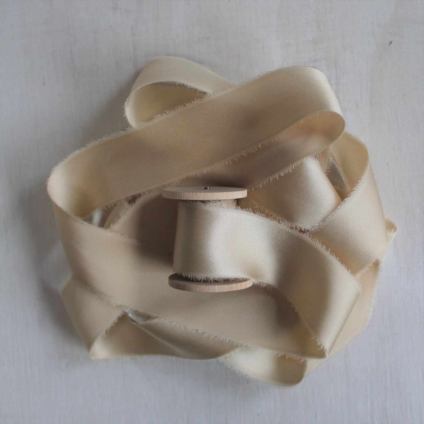 Close-up of maple silk charmeuse ribbon, hand-torn with feathered edges, showcasing its subtle sheen.
