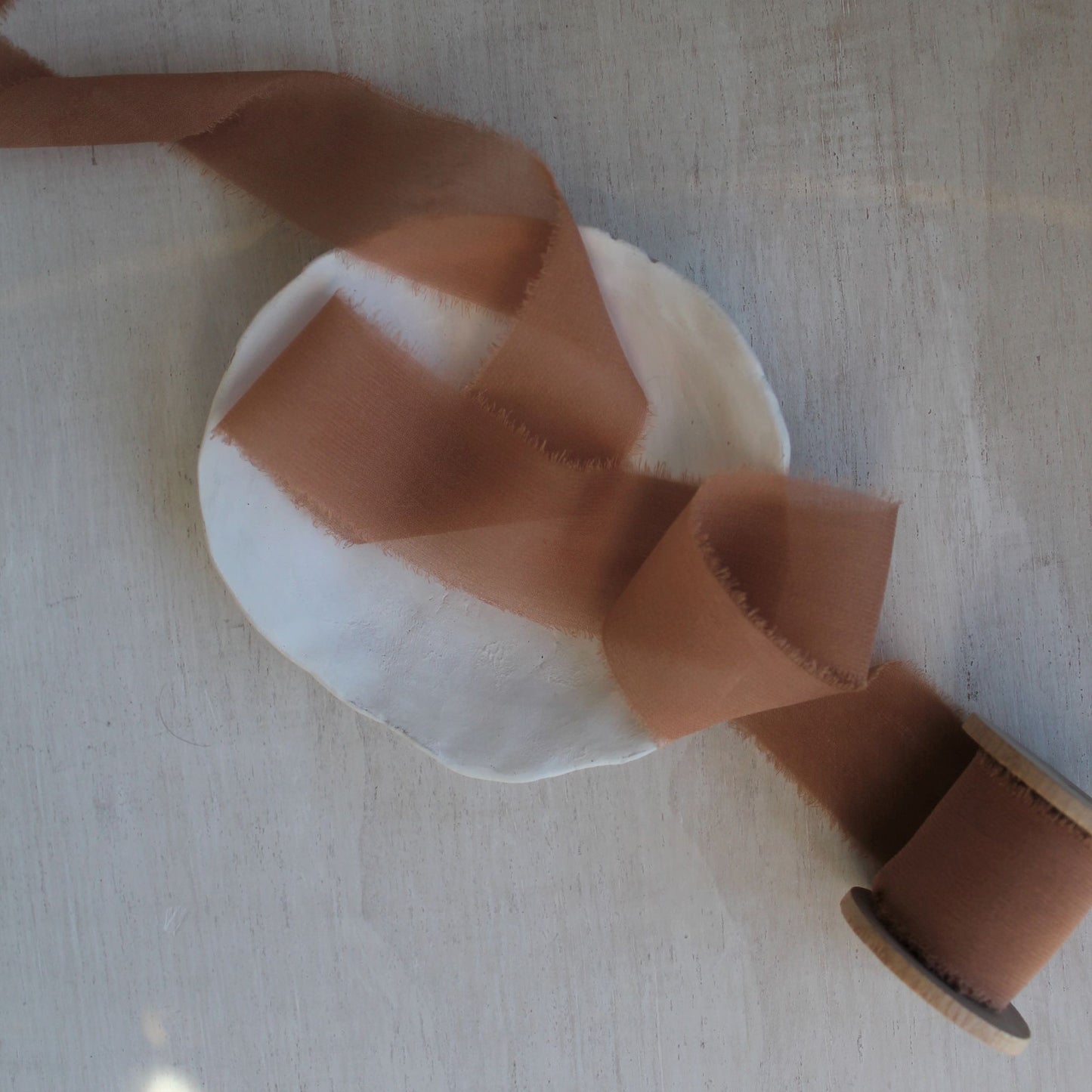 Terra cotta silk ribbon unspooled and flowing across table