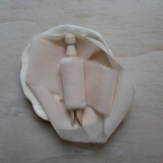 Pale pink hand-torn silk chiffon ribbon wound on a wooden clothespin, showcasing its delicate texture and soft hue.
