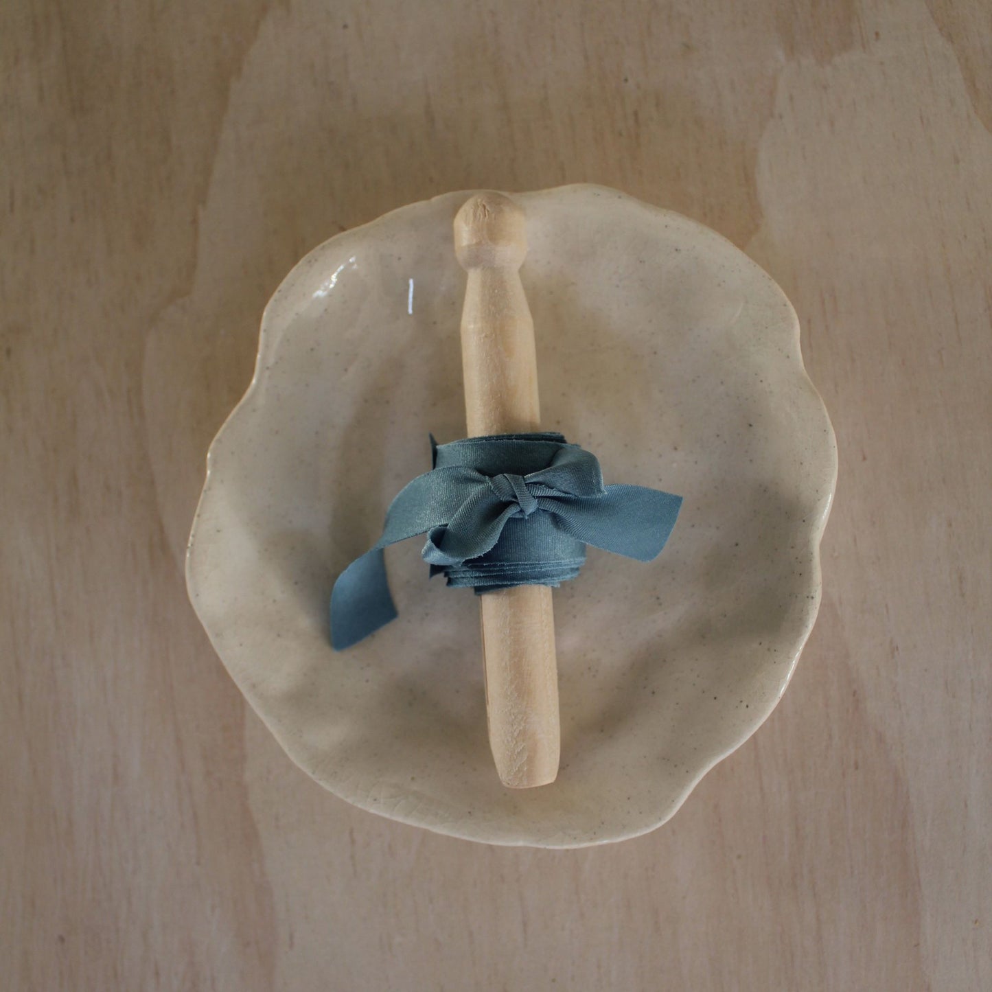 Beautifully styled handmade beige dish with a rolling pin wrapped in blue silk ribbon, perfect for elegant table settings.