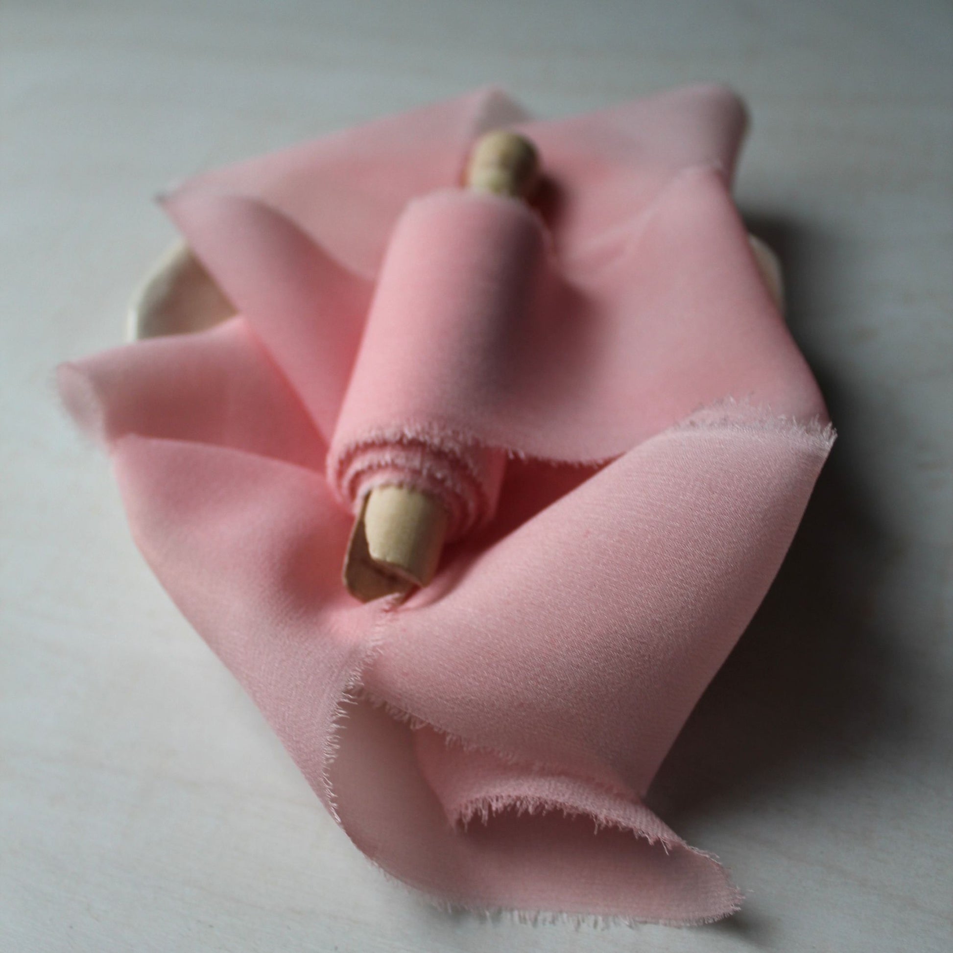 Soft iridescent pink chiffon ribbon with a delicate hand-torn finish, ideal for creating romantic wedding decor and invitations.