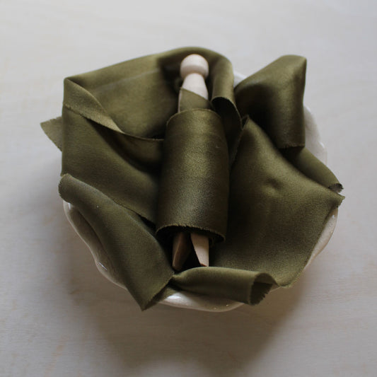Dark moss silk charmeuse ribbon styled flat on wood background