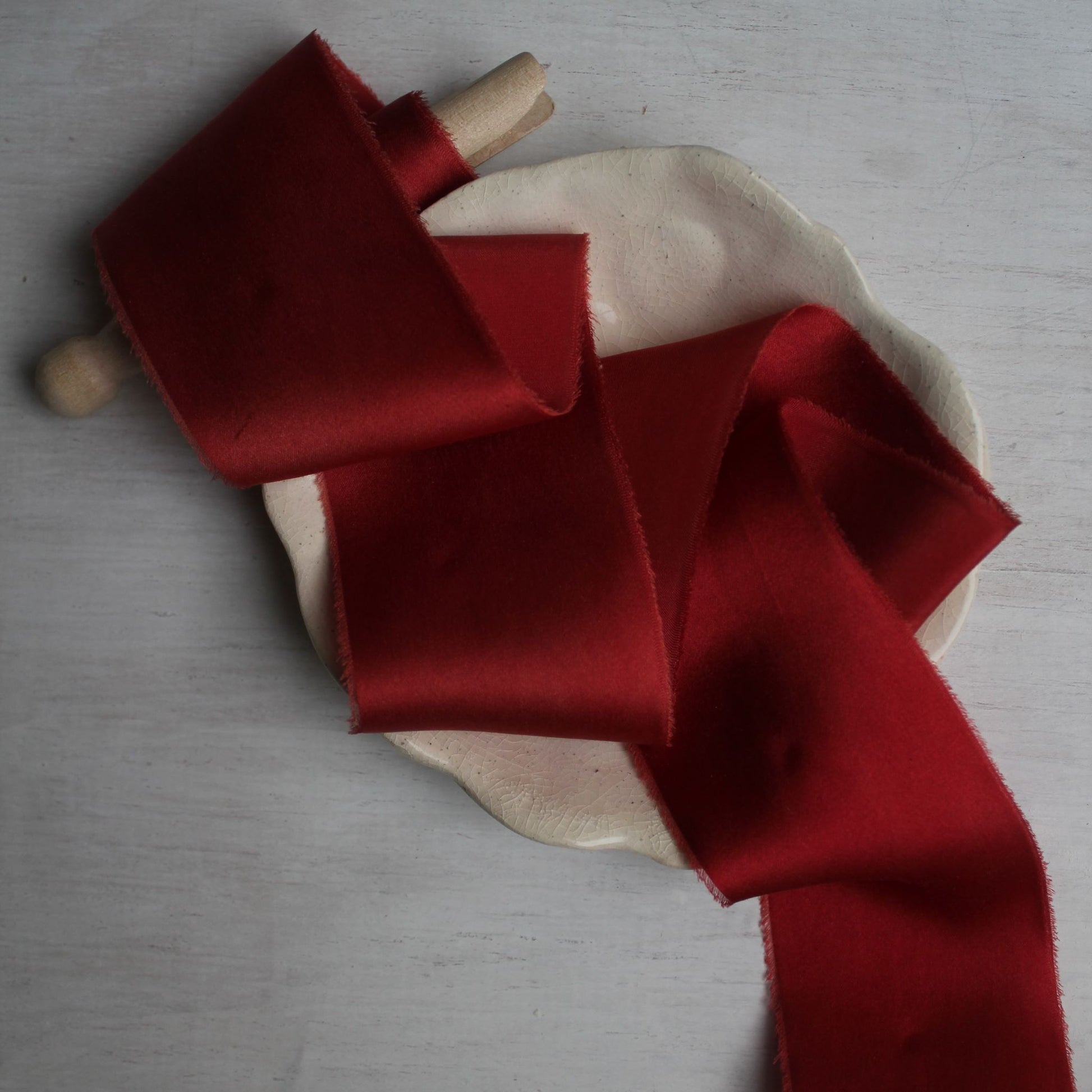 Hand torn Christmas red silk charmeuse ribbon on a beige plate, perfect for weddings and stationery.