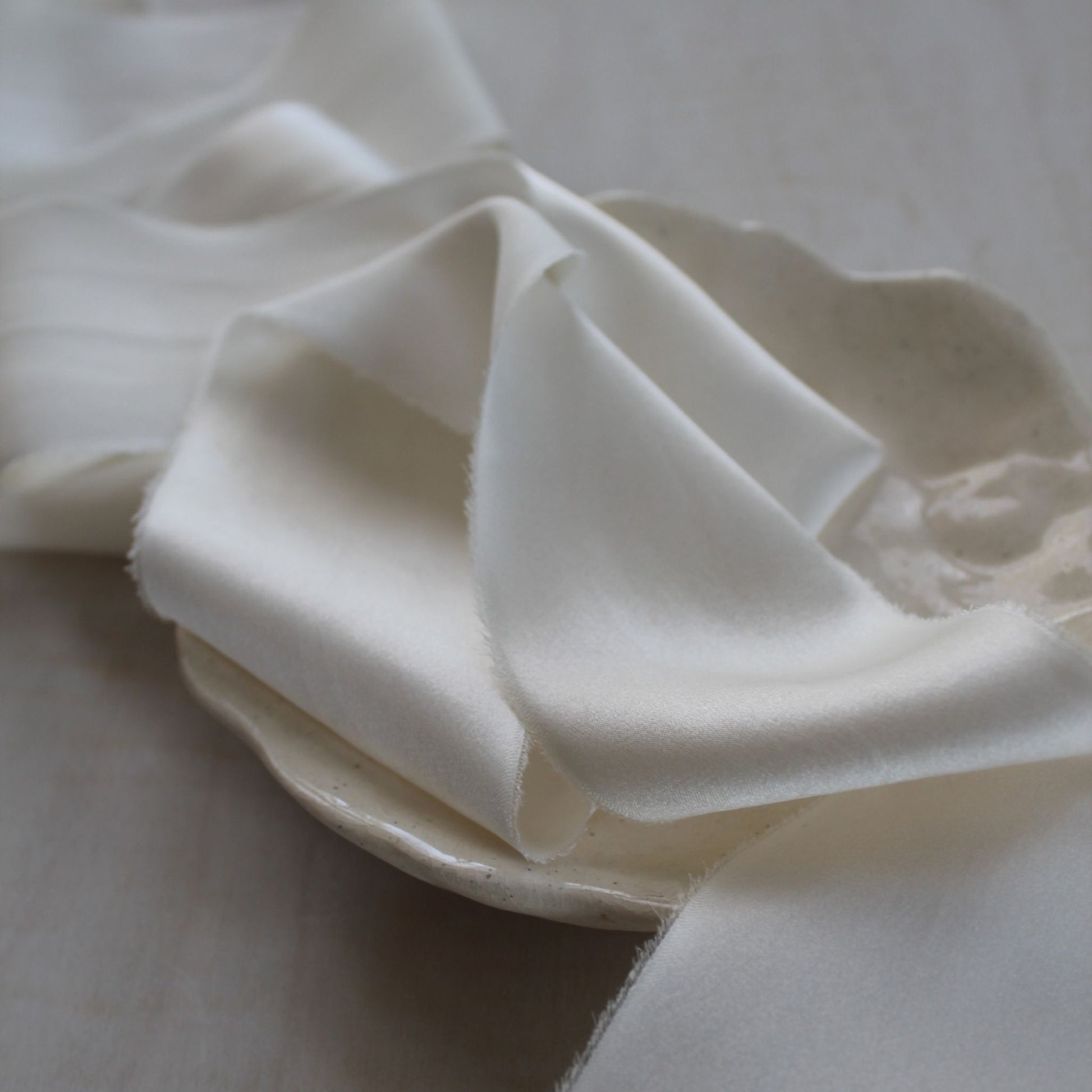 Close-up of hand-torn silk ribbon with frayed edge in soft white tone