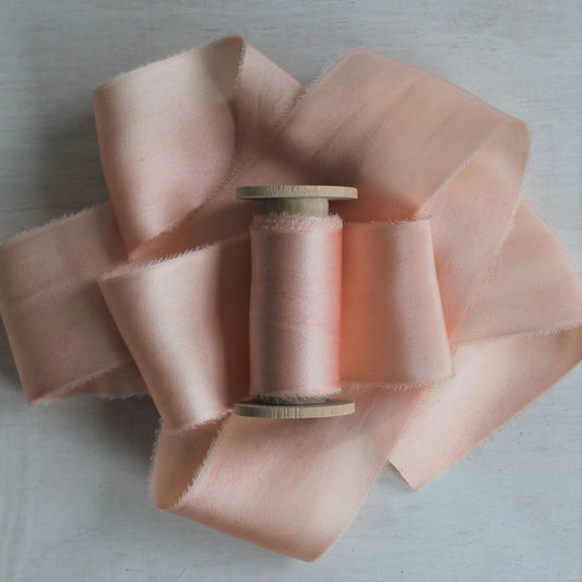 Pink blush silk charmeuse hand-torn ribbon on wooden spool.