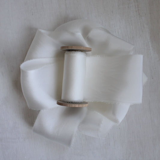 Hand-torn white silk charmeuse ribbon wound on a wooden spool, showcasing its soft sheen and frayed edges