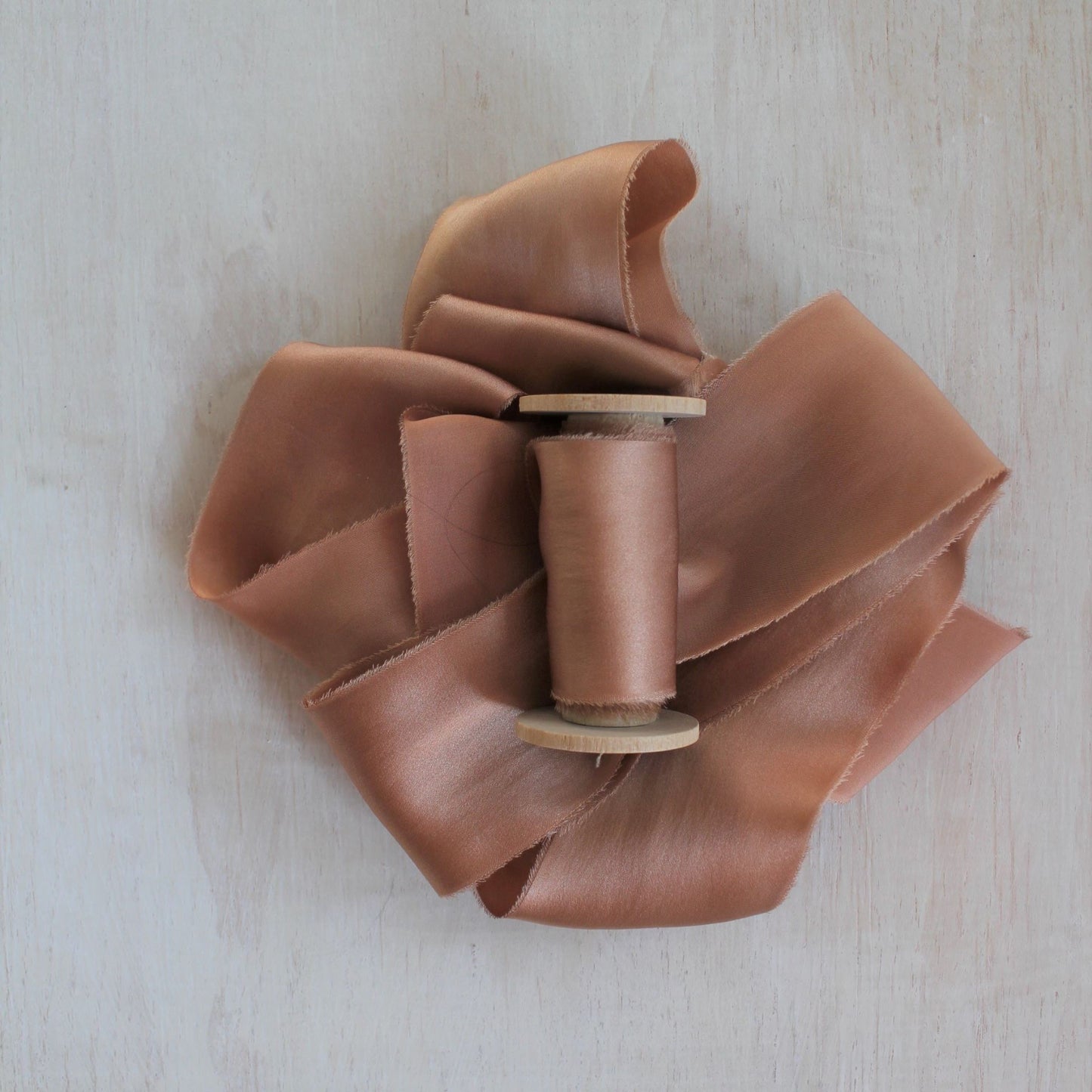 Hand-torn apricot silk charmeuse ribbon displayed on a wooden background