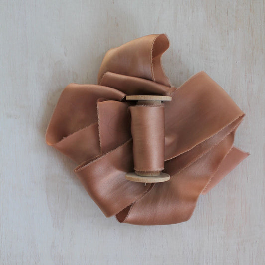 Hand-torn apricot silk charmeuse ribbon displayed on a wooden background
