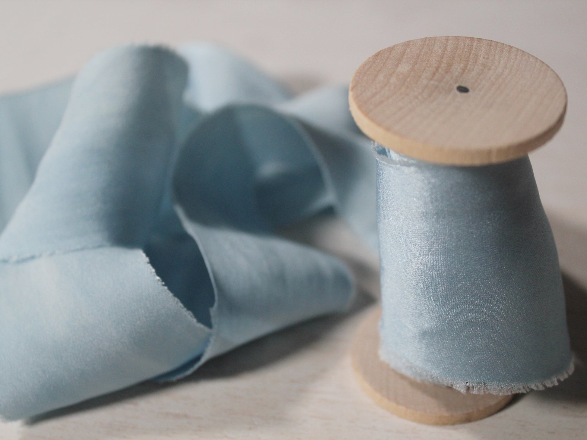 Bias-cut silk charmeuse ribbon in light blue, wrapped around a vintage-style wood spool