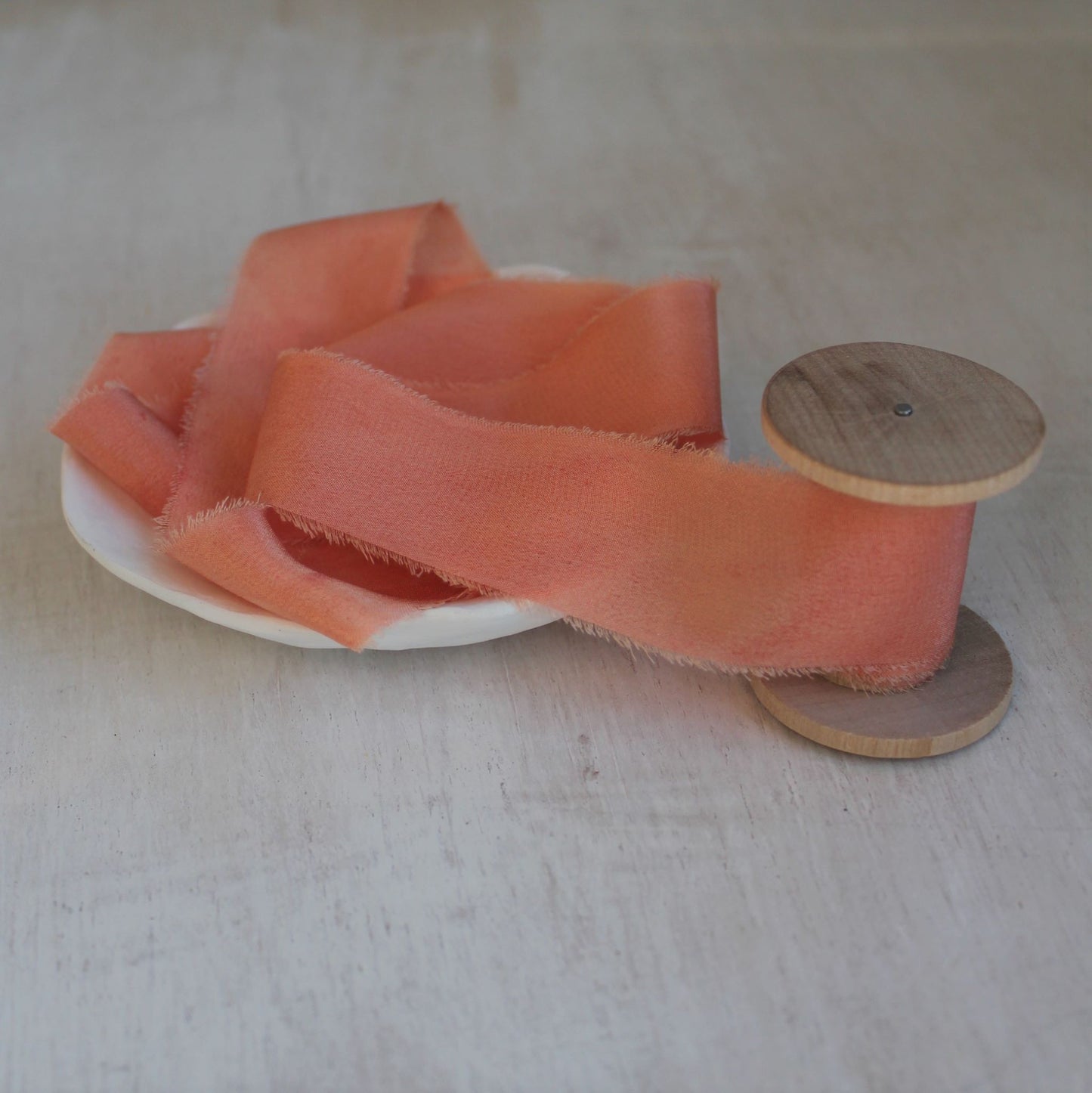 Bright pink silk crepe de chine ribbon placed on a wooden spool.