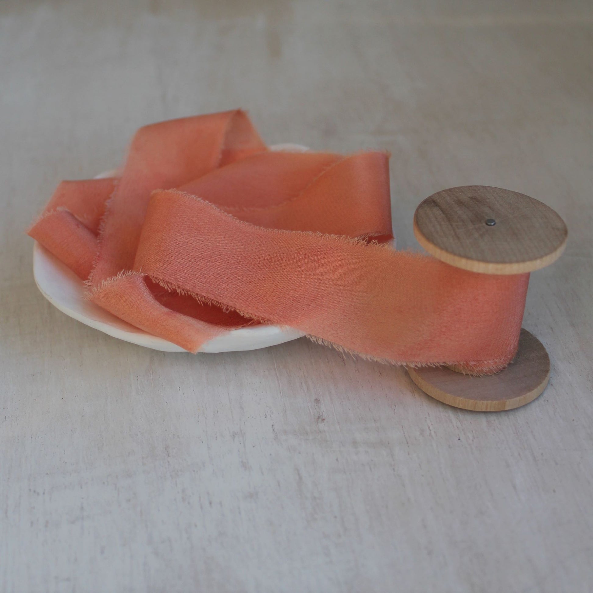 Bright pink silk crepe de chine ribbon placed on a wooden spool.
