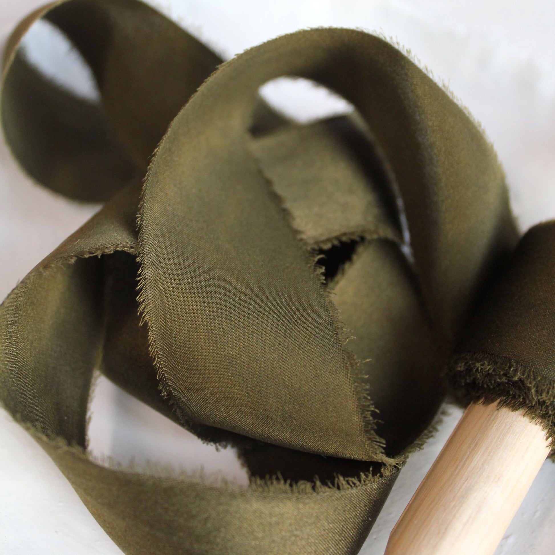 Close-up of hand-torn dark moss silk charmeuse ribbon showcasing feathered edges.