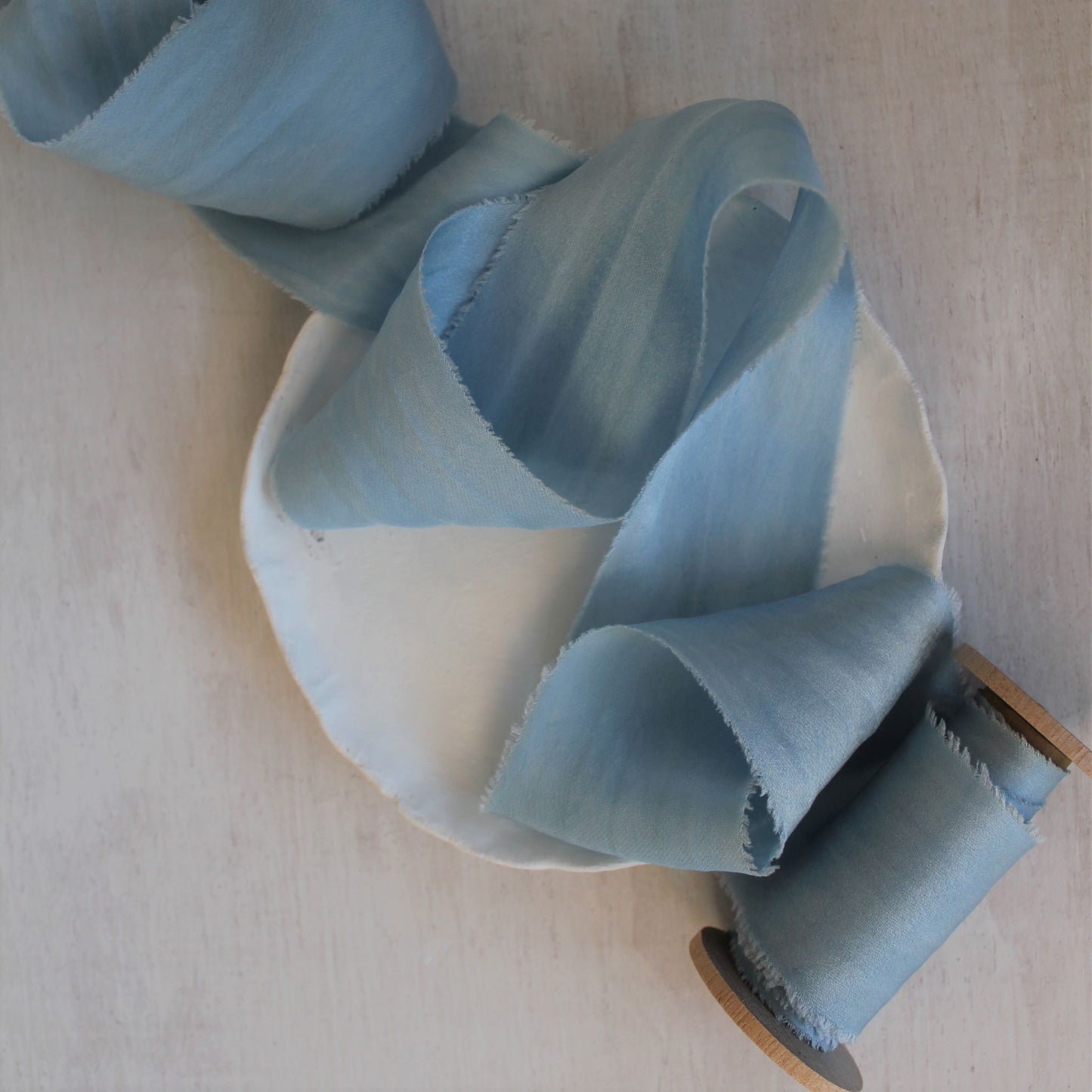 Soft silk ribbon in pale blue displayed on a wood spool, highlighting the ribbon's subtle shine.