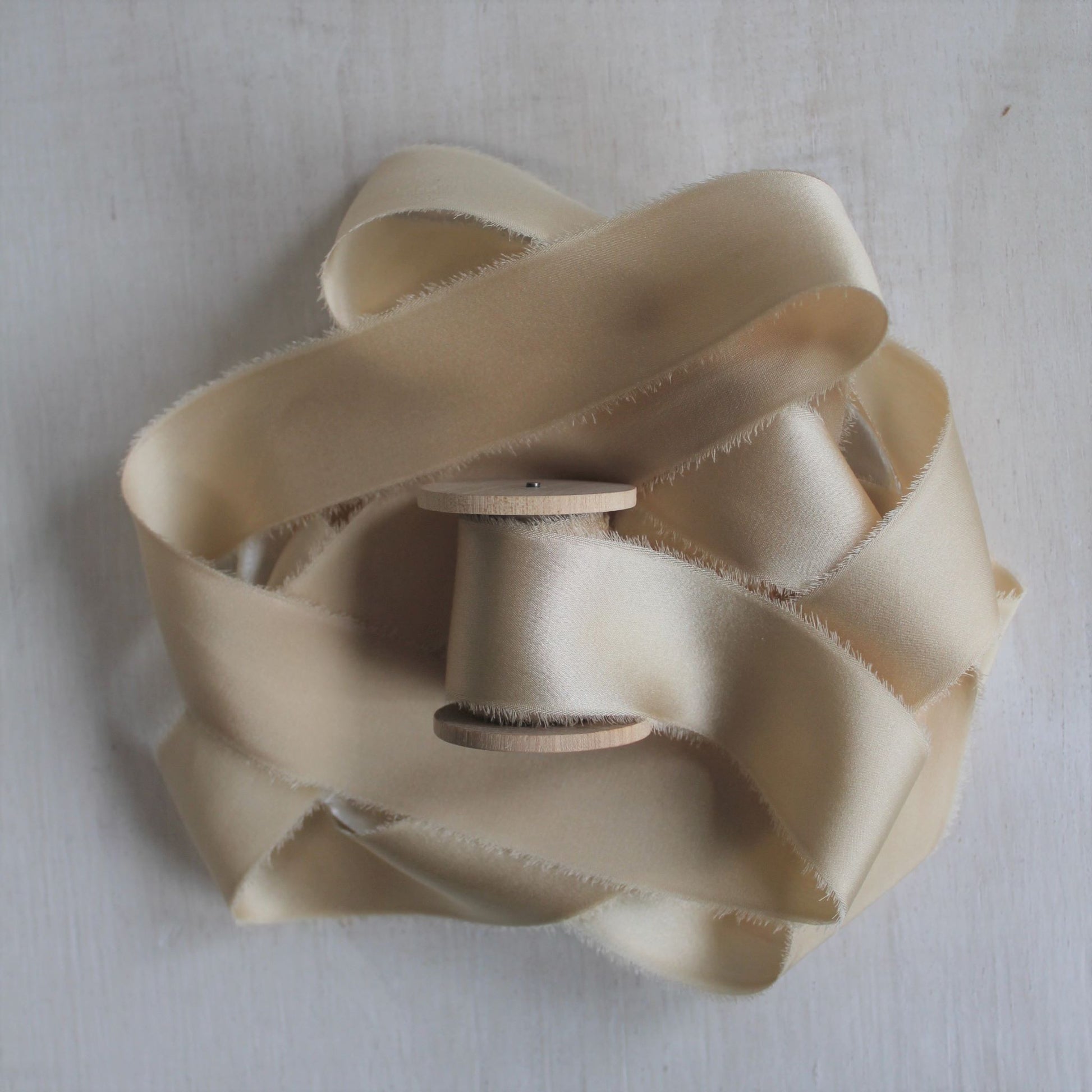 Close-up of maple silk charmeuse ribbon, hand-torn with feathered edges, showcasing its subtle sheen.