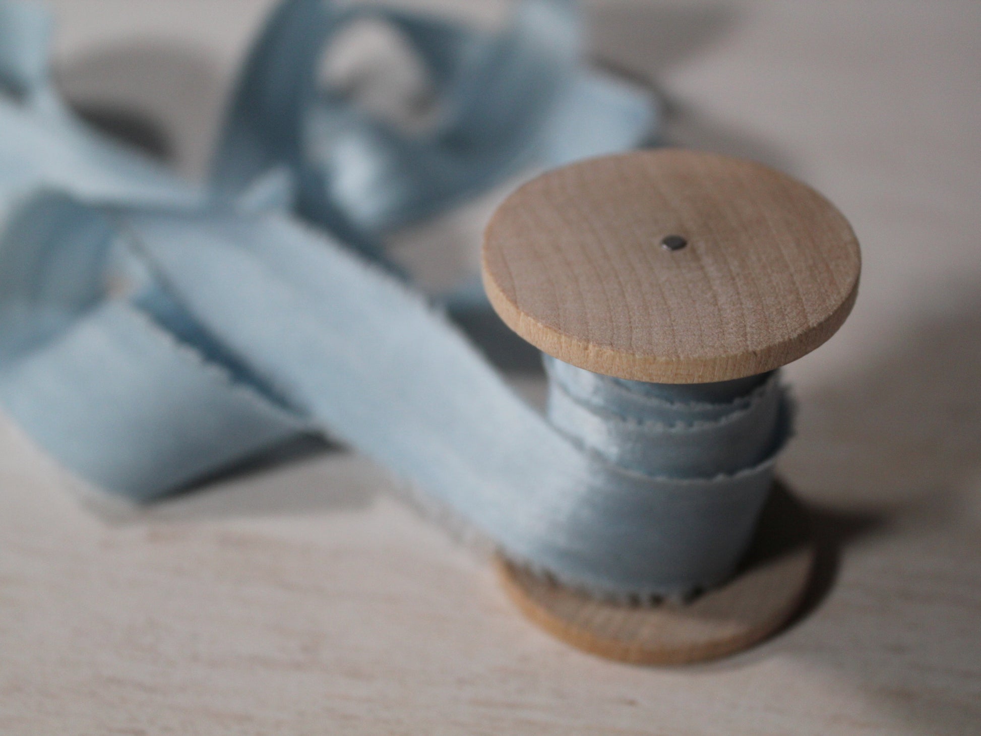 Soft silk ribbon in pale blue displayed on a wood spool, highlighting the ribbon's subtle shine