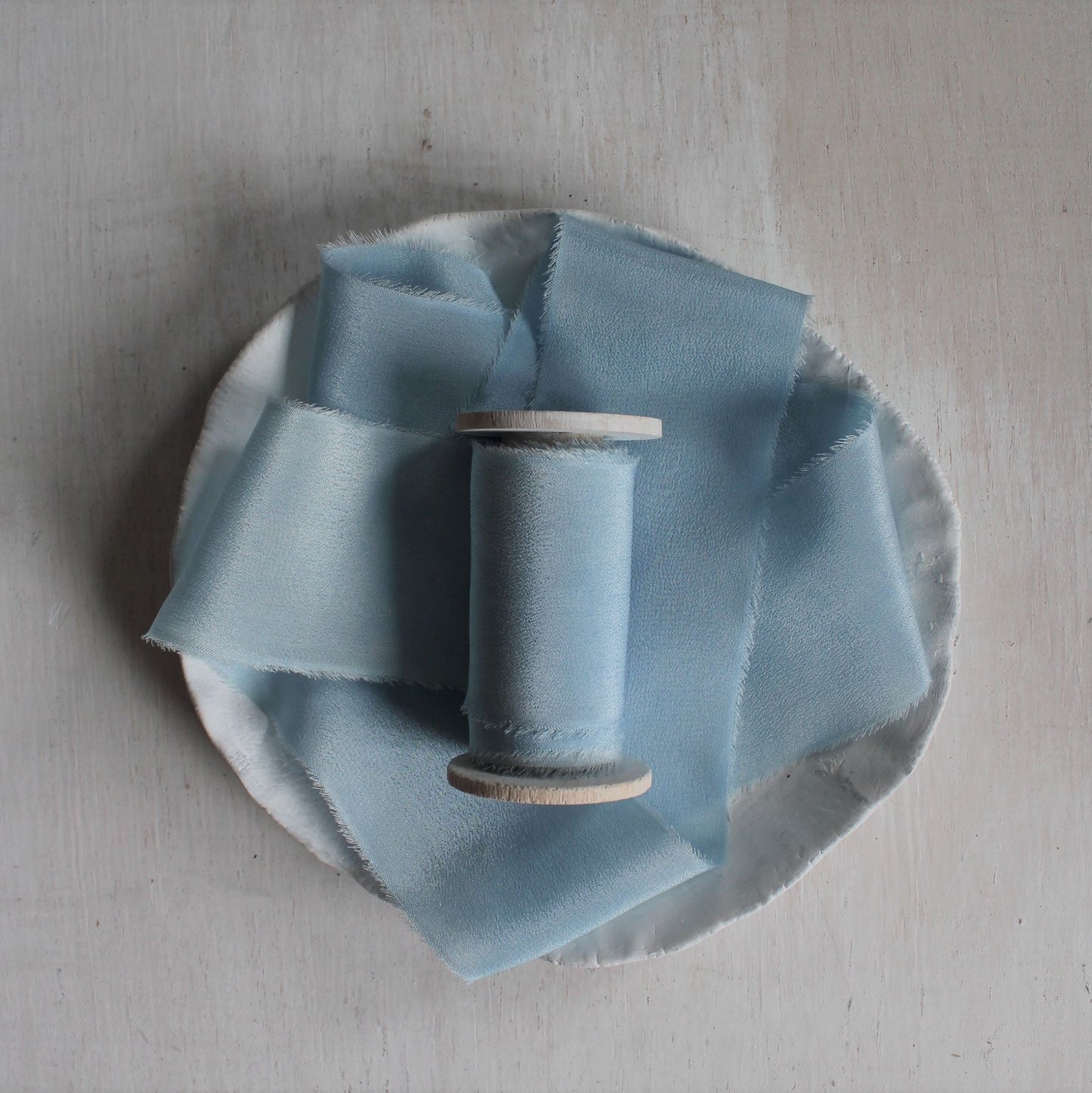 Pale blue silk ribbon hand torn and naturally dyed with indigo, displayed on wood