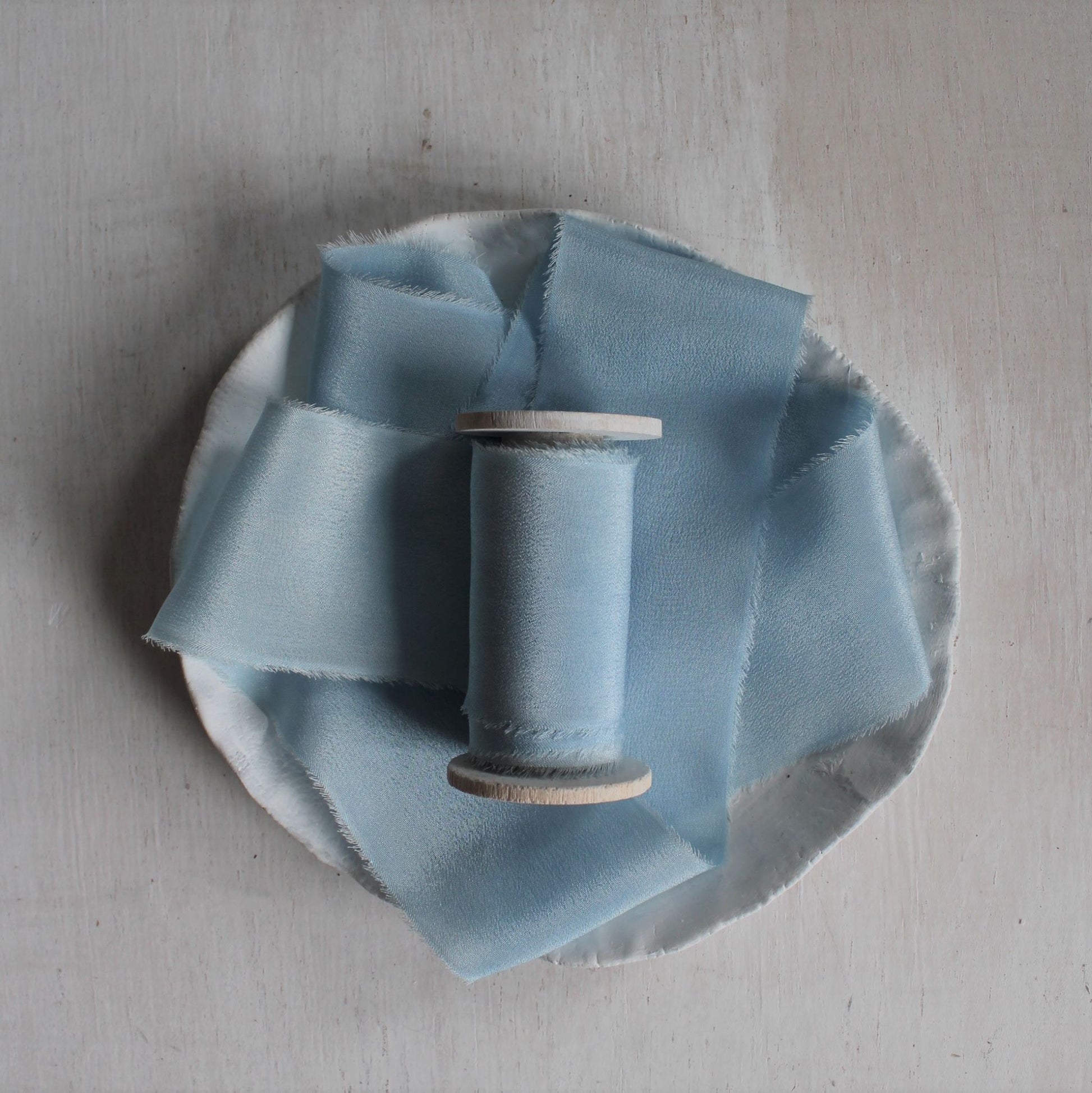 Pale blue silk ribbon hand torn and naturally dyed with indigo, displayed on wood