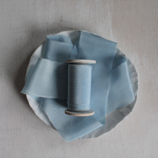 Pale blue silk ribbon hand torn and naturally dyed with indigo, displayed on wood