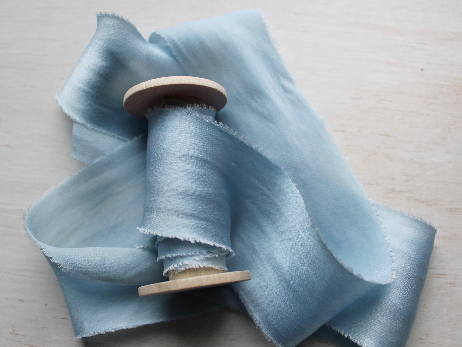 Pale blue silk charmeuse ribbon coiled neatly, emphasizing its seamless, handcrafted quality