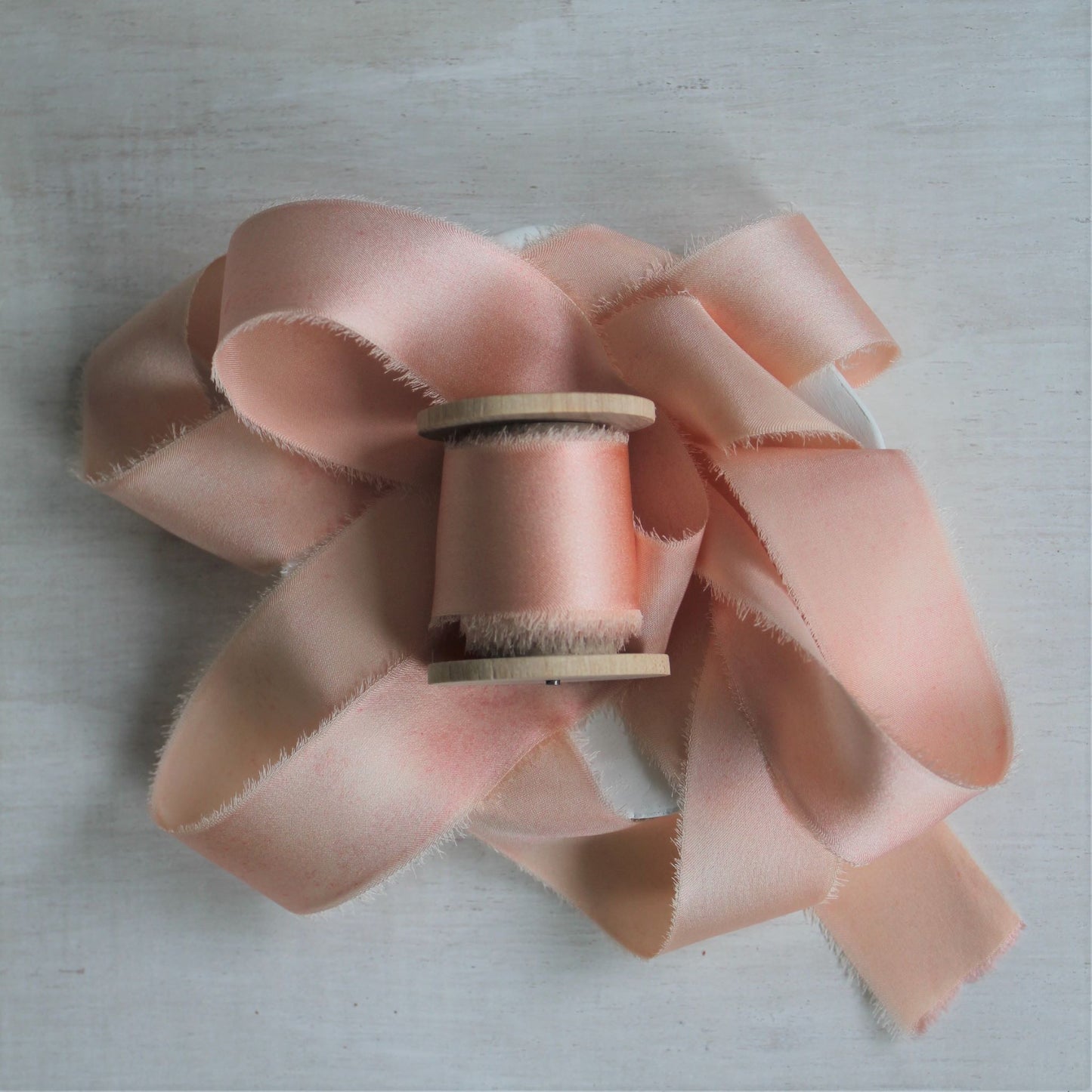 Pink blush silk charmeuse hand-torn ribbon on wooden spool.