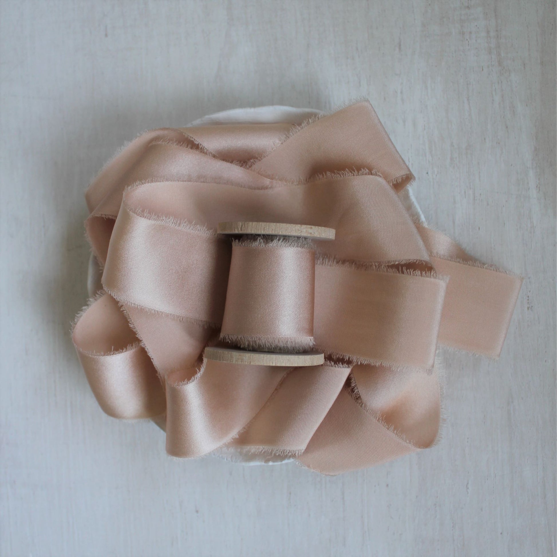 Hand-torn pink charmeuse silk ribbon on wood spool