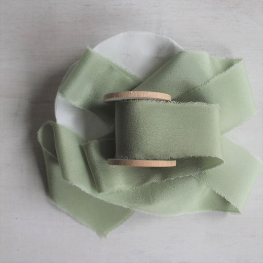 Hand-torn sage silk crepe de chine ribbon displayed on a wooden spool