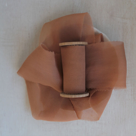 Soft, sheer terracotta silk ribbon styled for product photography