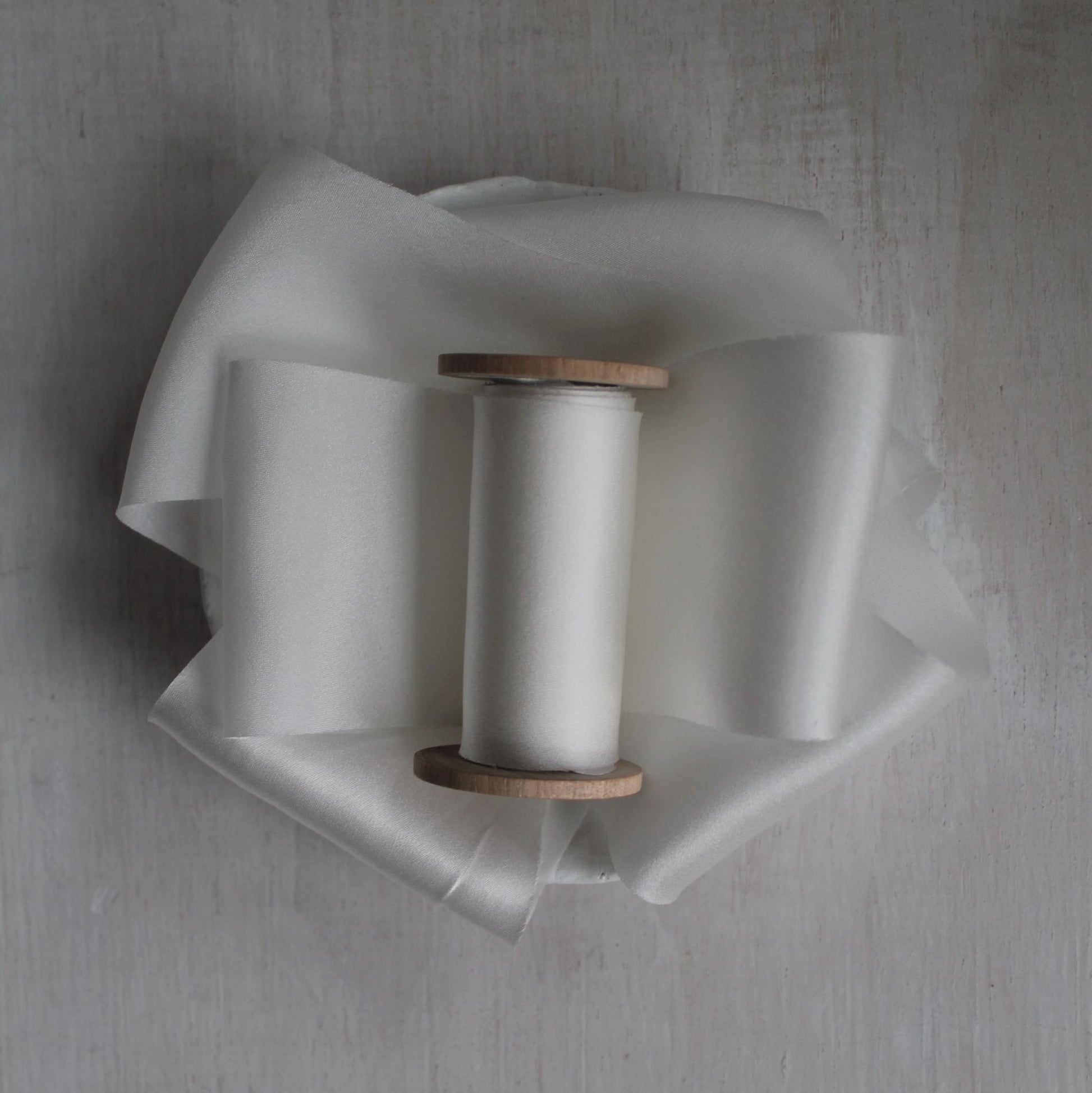 White bias cut silk charmeuse ribbon on wood spool