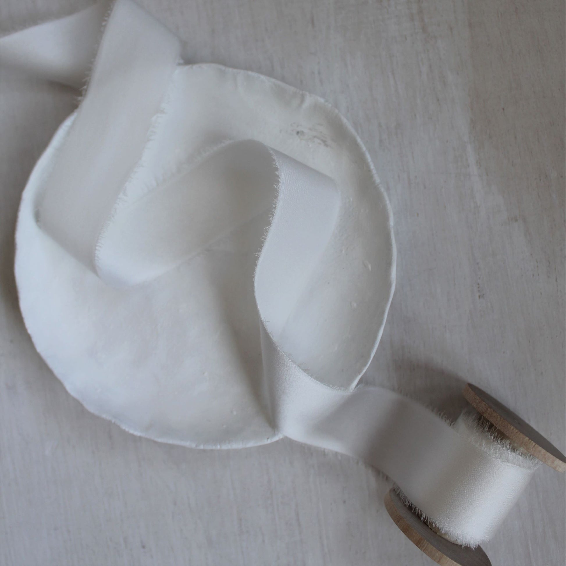 White silk ribbon draped gracefully over a wooden surface, demonstrating its soft drape and sheen
