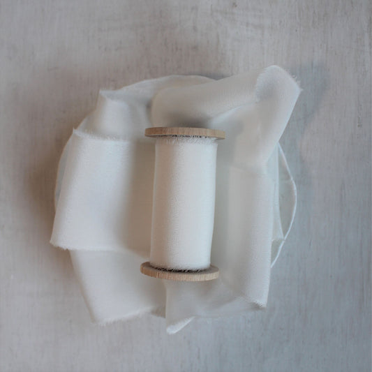 Hand-torn white silk crepe de chine ribbon displayed on a wooden spool