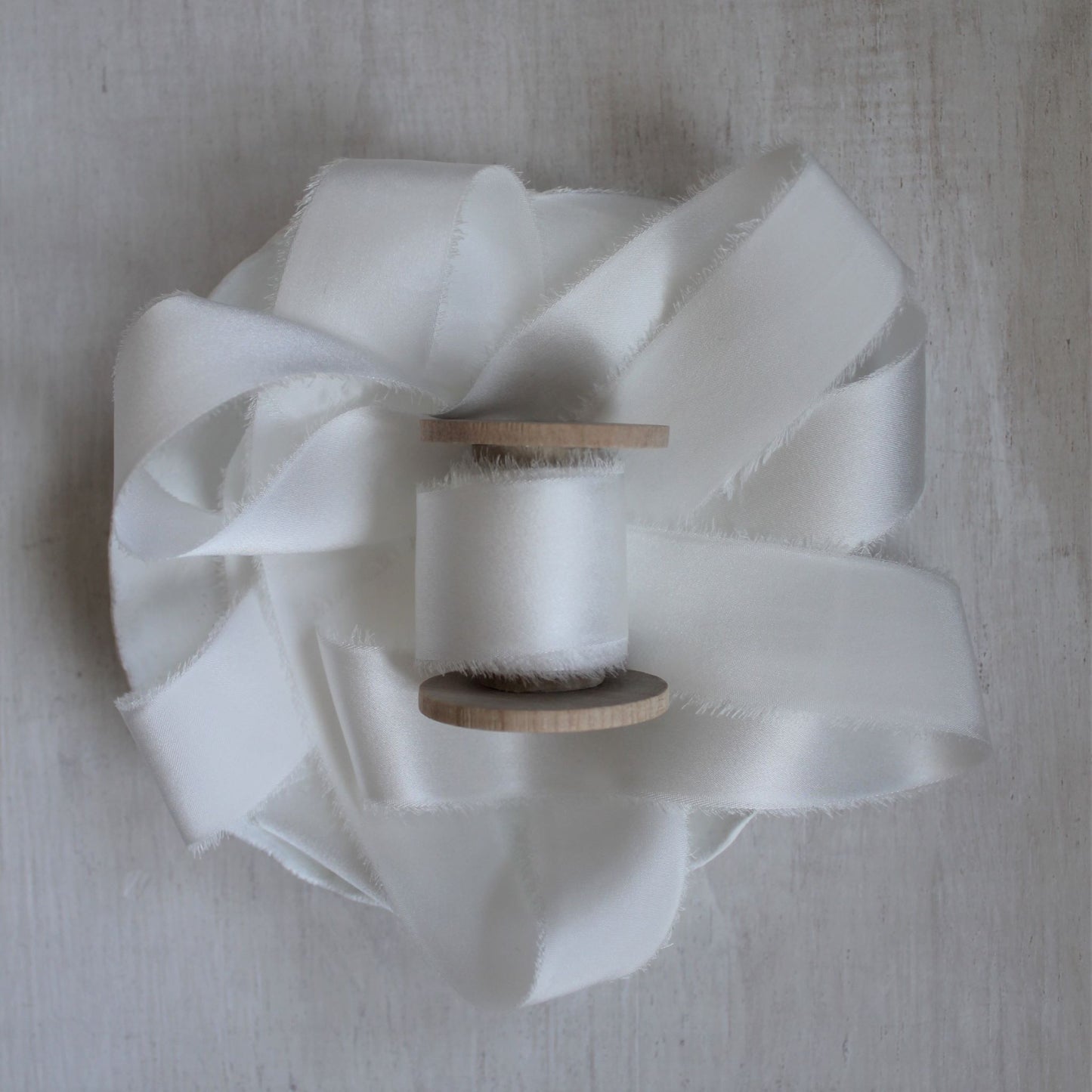 Close-up of frayed edge on hand-torn silk charmeuse ribbon, showing texture and craftsmanship