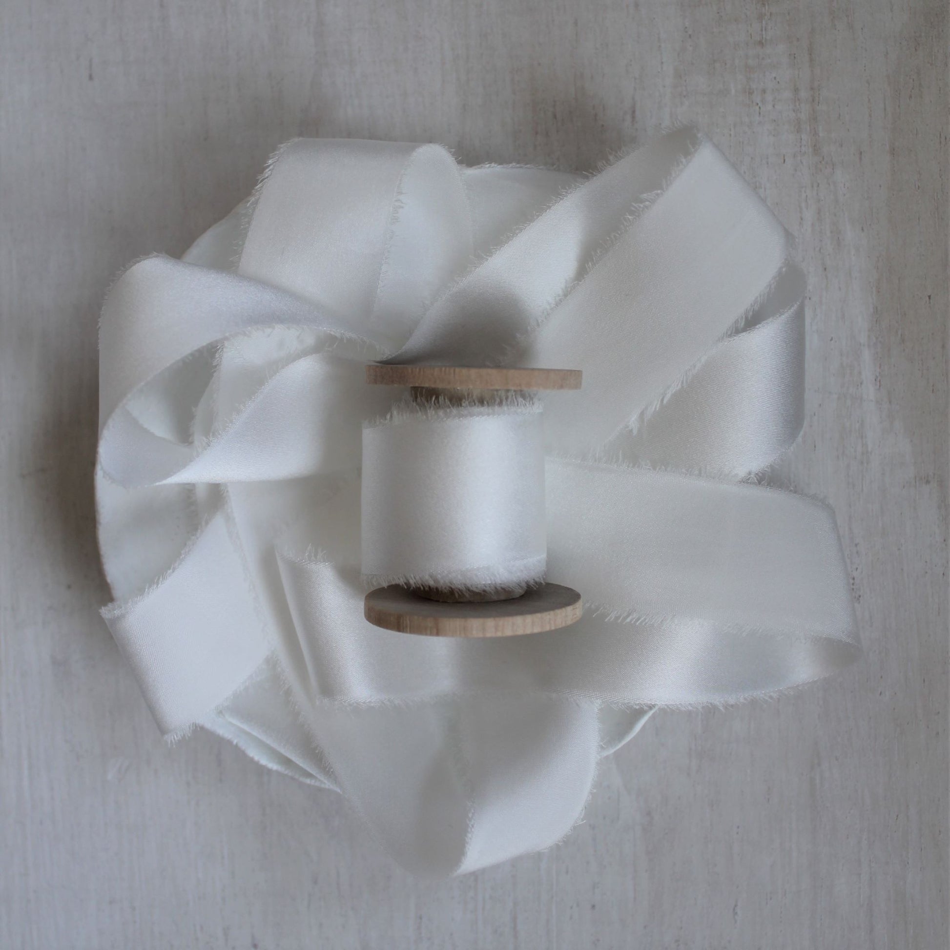 Close-up of frayed edge on hand-torn silk charmeuse ribbon, showing texture and craftsmanship