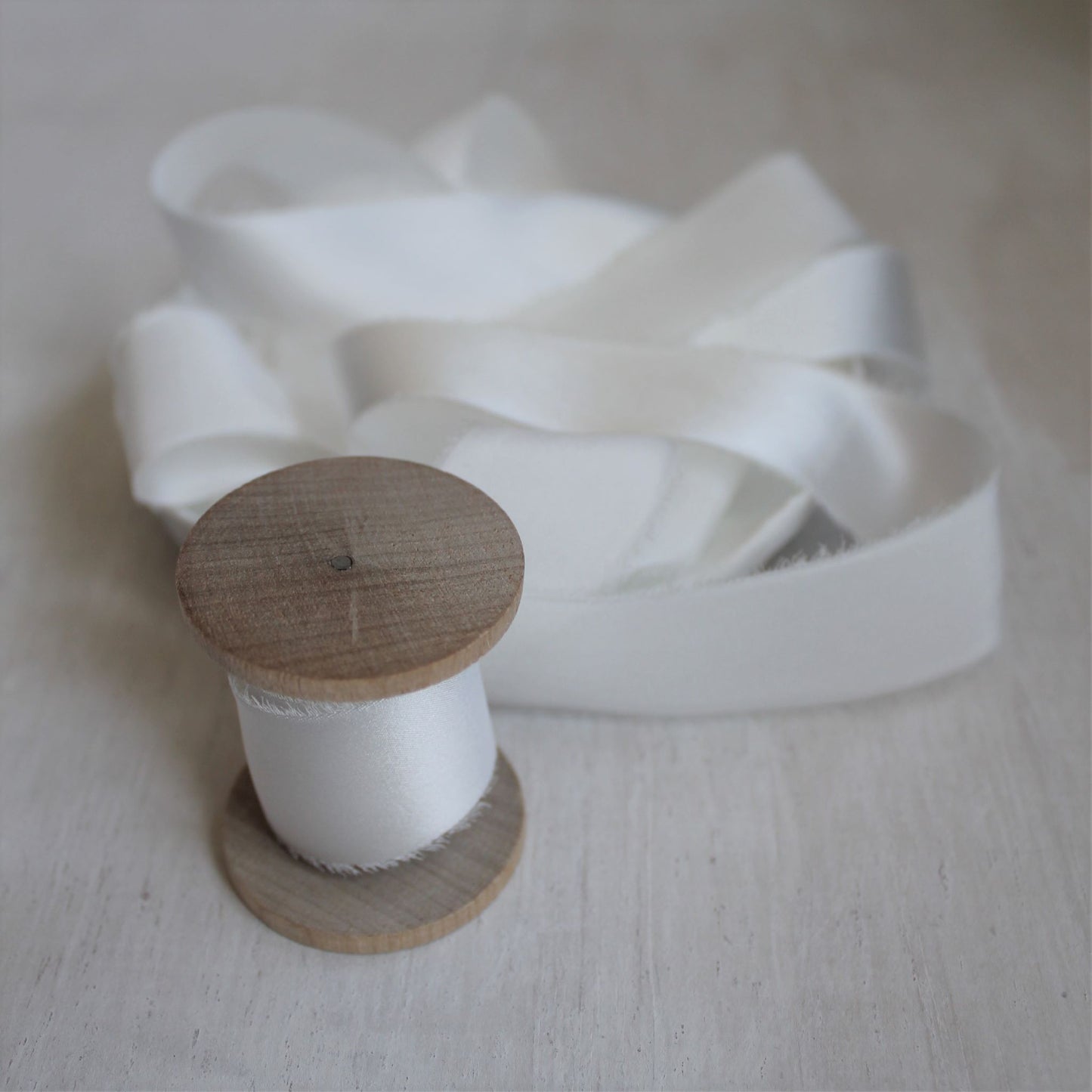 Hand-torn white ribbon photographed on a rustic wood backdrop, evoking vintage wedding charm